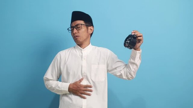 Asian muslim man feeling hungry while holding a clock in ramadan season fasting concept