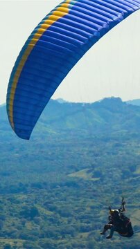 Super slow motion. Two People ride Paramotor paraglide paraplane flying in the sky with mountains midday sunny. Blue clouds. Vertical shot.