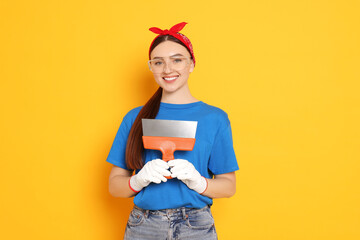 Portrait of young decorator with putty knife on orange background