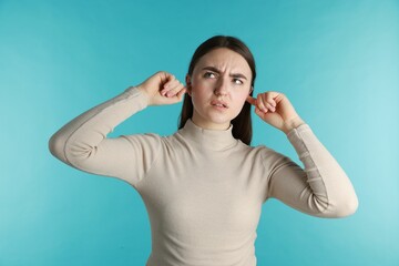 Frustrated woman covering her ears from loud noise on blue background