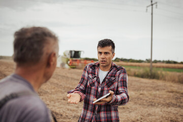 Upset farmer in soybean field talking to other man during harvest