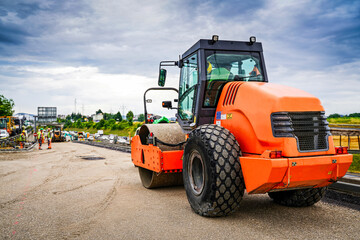 Close-up of an asphalt compaction roller on a highway construction site during a sunny day, showcasing details of the machinery and the paving process.