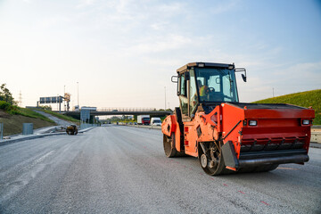 Close-up of an asphalt compaction roller on a highway construction site during a sunny day, showcasing details of the machinery and the paving process.