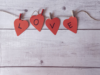Red heart pattern with letters L, O, V, E. Forming the word love in English. On white wooden background.