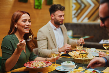 Cheerful business colleagues enjoying a delicious meal and white wine during their lunch break at a...