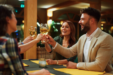 Happy friends are toasting with white wine, enjoying an evening together in a restaurant