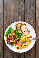 Continental breakfast - scrambled eggs with bacon, slices of bread and fresh salad on wooden table