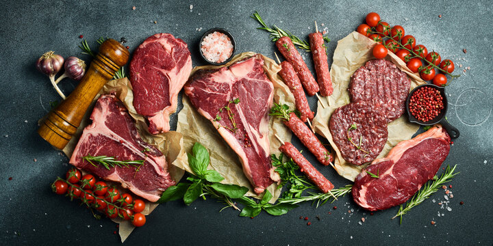 A set of juicy raw steaks, kebabs, cutlets and meat with spices and herbs. On a black stone background. Top view.