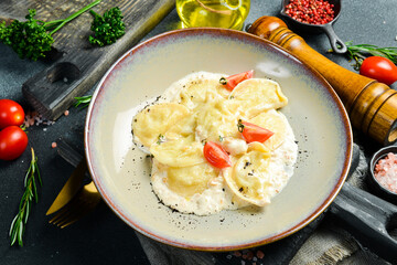 Ukrainian cuisine: potato dumplings with cream sauce. In a plate. Homemade food. On a dark stone background.