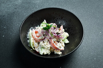 Salad of cabbage, tomatoes, onions and radish dressed with sour cream. On a plate. Restaurant serving. Close up. On a dark stone background.