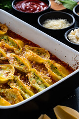 Pasta shells stuffed with cheese and spinach with tomato sauce in baking dish on black table