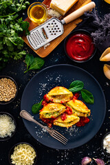 Pasta shells stuffed with cheese and spinach with tomato sauce on black table