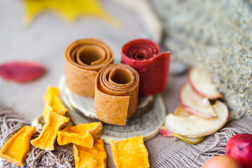 Freshly rolled, homemade fruit leather and dried fruit slices made from organic ingredients are displayed on a rustic table