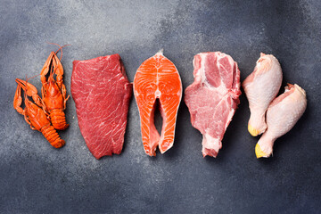 Set of various raw meats on a dark grunge background. beef, fish, lobster claws, pork and chicken. Free space for text. On a gray stone background.