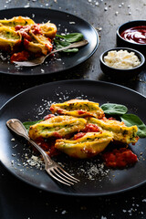 Pasta shells stuffed with cheese and spinach with tomato sauce on black table