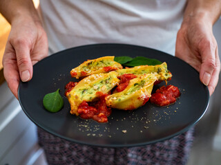 Woman holding plate with pasta shells stuffed with cheese and spinach with tomato sauce