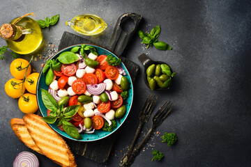 Fresh summer salad: tomatoes, mozzarella cheese, basil and olives. Caprese. On a gray concrete background.