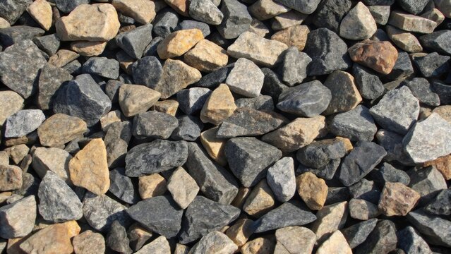 A detailed view of crushed stone ballast the jagged edges of the rocks glinting in the sunlight. The various shades of gray black and tan create a natural mosaic each stone