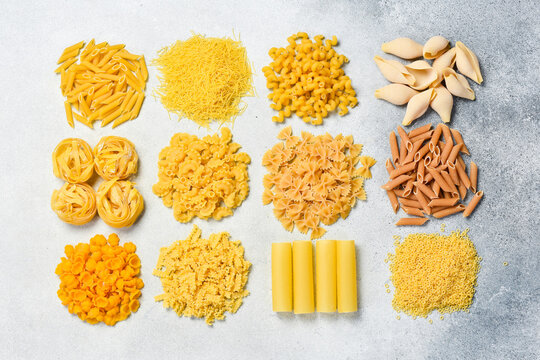Different kinds of raw pasta on gray stone background. Top view.