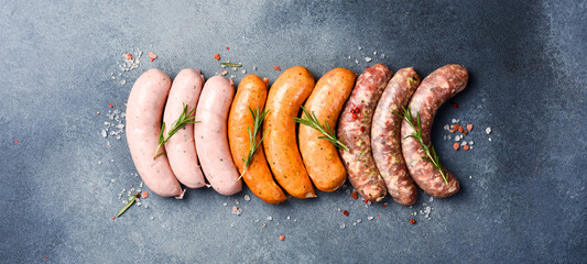 Uncooked mix of barbecue sausages: beef, pork and chicken sausages. On a gray concrete background....