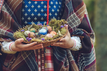 Woman in traditional Lithuanian clothes holding basket filled with Easter eggs