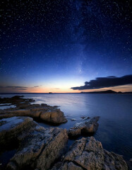 A sunset with vibrant colors over a calm water, featuring a rock
