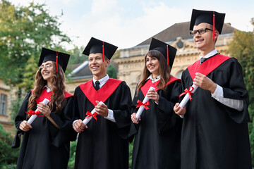 Happy students with diplomas after graduation ceremony outdoors