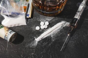 White narcotic pills, an alcoholic drink in a glass, a syringe with a dose of heroin, a line of...