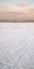 Snow-covered beach at sunrise with gentle waves and cloudy sky