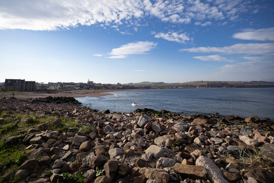 Coastal view of Stonehaven, Scotland during a clear day with rocky shoreline and distant cityscape