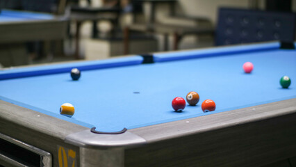 A close-up view of a blue pool table with a variety of colored billiard balls scattered across its surface.