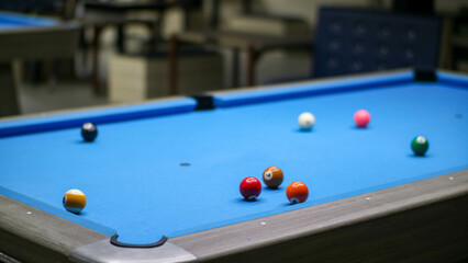 A close-up view of a blue pool table with a variety of colored billiard balls scattered across its surface.