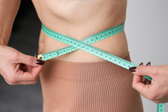 Woman measuring her waist circumference with a measuring tape. Very thin waist background. Obsession with weight and body image. Anorexia and unhealthy body perception. Visible ribs woman body.