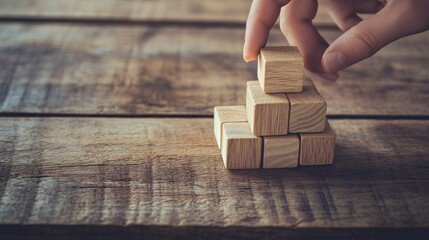 A close-up of a hand stacking wooden blocks on a rustic wooden table, symbolizing creativity and construction.