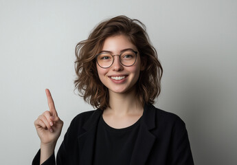 Portrait of a happy young woman wearing glasses, smiling and pointing her finger upward, isolated on a white background. 