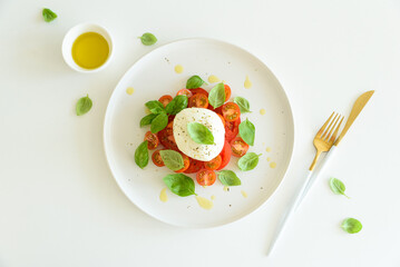 Salad Caprese with tomato, cherry, mozzarella and basil leaves on white wooden table