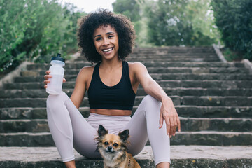 Cheerful black woman having fun with cute dog in forest
