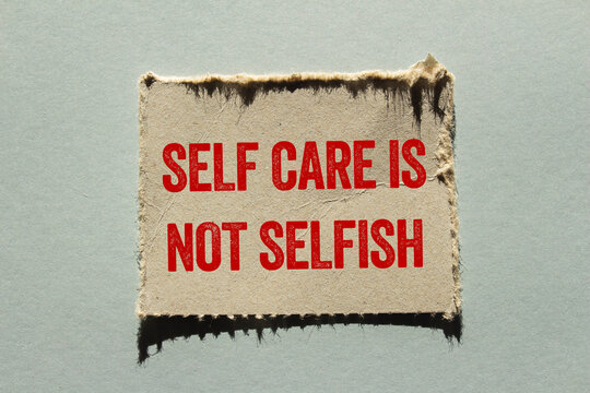 Self care is not selfish message written on ripped torn paper piece on gray background. Conceptual self care is not selfish symbol. Copy space.