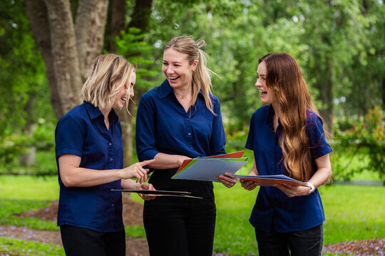Three female speech pathologists holding phonics resources chatting together 