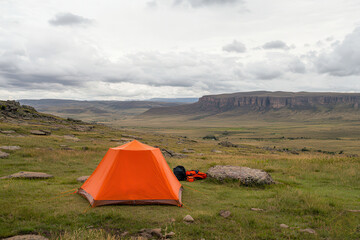 Outdoor adventures and camping promote sustainability. Orange tent in a vast, grassy landscape under cloudy sky.