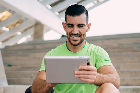 Cheerful male in sportswear using digital tablet for browsing wireless information about workout training, happy Caucaisan athlete enjoying online messaging in social networks using touch pad - Powered by Adobe