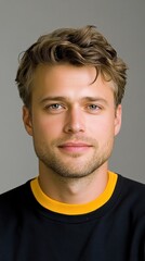 Fototapeta premium Young man with stylish curly hair and friendly smile, wearing black and yellow shirt, sitting against neutral background for portrait photography or professional use