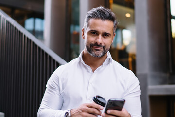 Half length of middle aged professional employee with cellular gadget and coffee to go in hands...