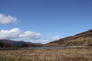 Fototapeta premium Scenic view of Scottish landscape featuring a tranquil lake and rolling hills under a clear blue sky