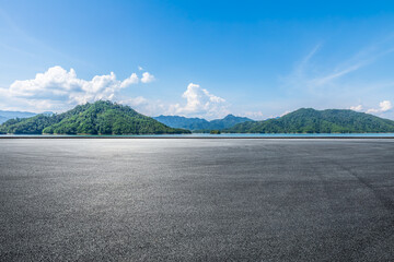 Asphalt road square and lake water with green mountain nature landscape under blue sky. Outdoor asphalt parking lot.