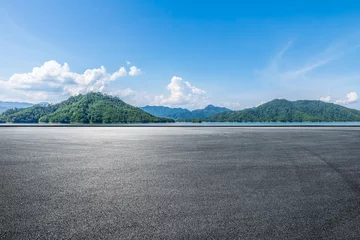 Fototapete Asphalt road square and lake water with green mountain nature landscape under blue sky. Outdoor asphalt parking lot. © ABCDstock