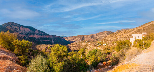 Majestic panorama showcasing the rugged beauty of Atlas mountains in Morocco, with lush vegetation and traditional houses nestled amidst the slopes, under a vibrant blue sky