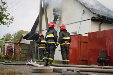 Firefighters battling flames at a residential building during a cloudy day in a suburban...