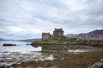 Historic castle ruins reflect on calm waters near the coast of Scotland under an overcast sky