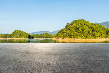 Asphalt road square and lake water with green mountain nature landscape under blue sky. Outdoor asphalt parking lot. © ABCDstock